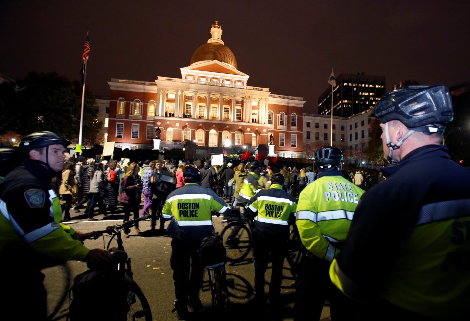  Local and state police watch as people march past the state house in protest against Donald Trump in Boston