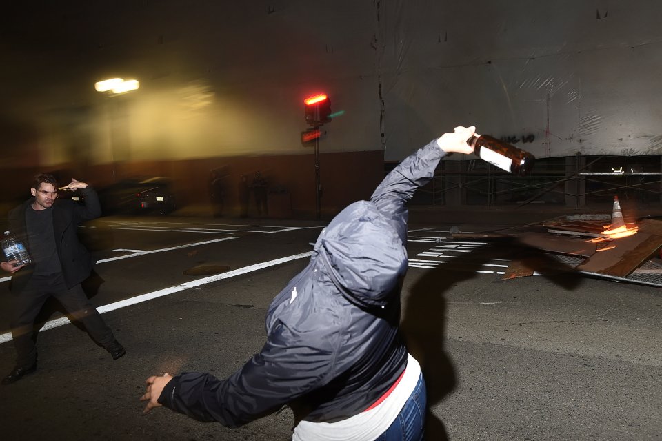  Anger... A protester throws a bottle at police officers following the election of Donald Trump