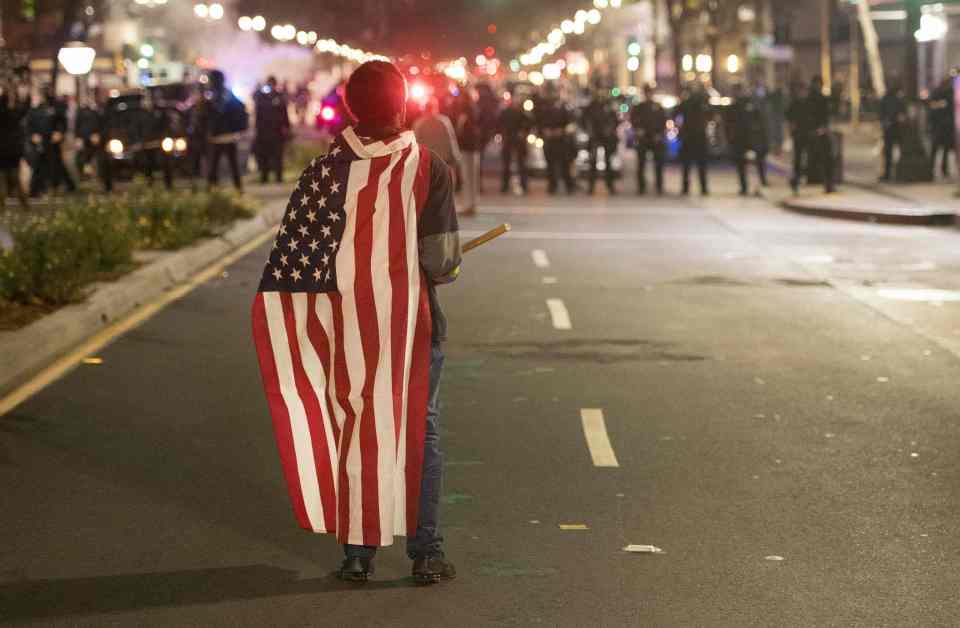  A protester wearing an American flag faces police