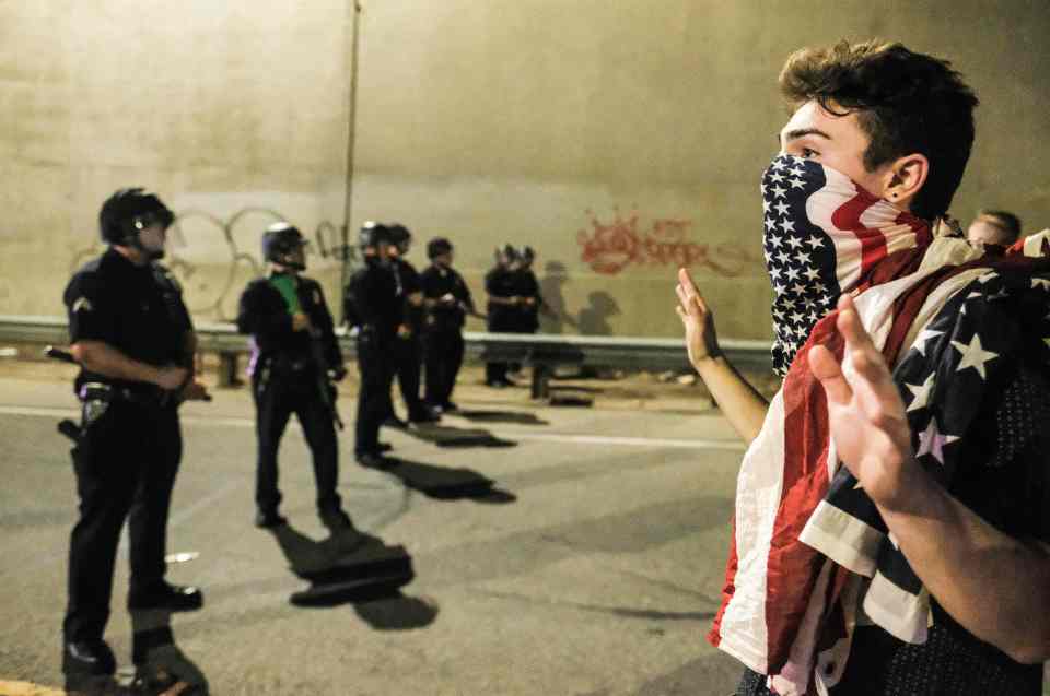  A protester using the US flag as a mask confronts police