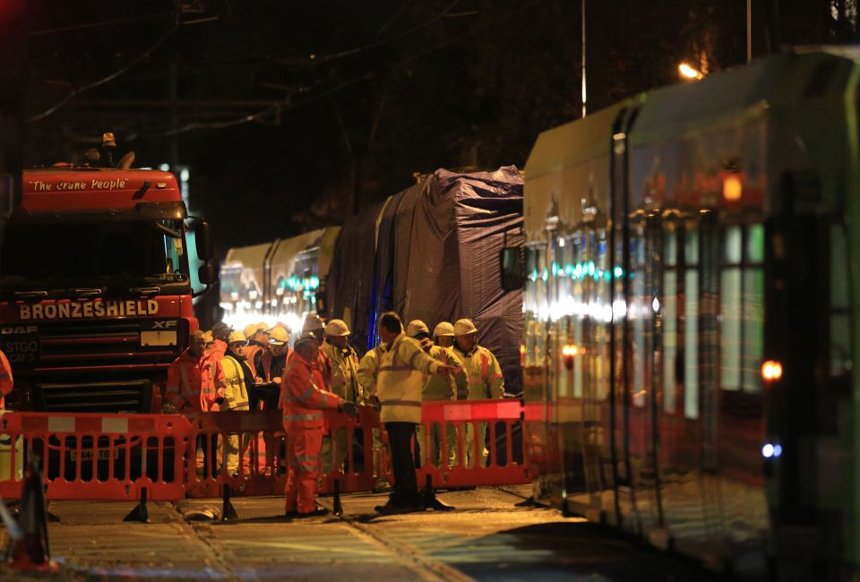  A damaged tram carriage is seen wrapped in tarpaulin as preparations are made to remove it from the scene