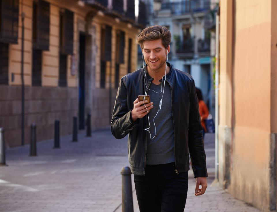 This is a very common sight - a young man listening music with smartphone earphones walking in the street