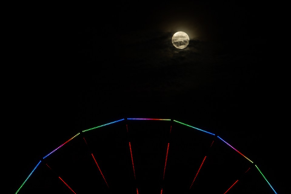  The larger, brighter full moon peeps through clouds above a ferris wheel in Aberdeen this evening