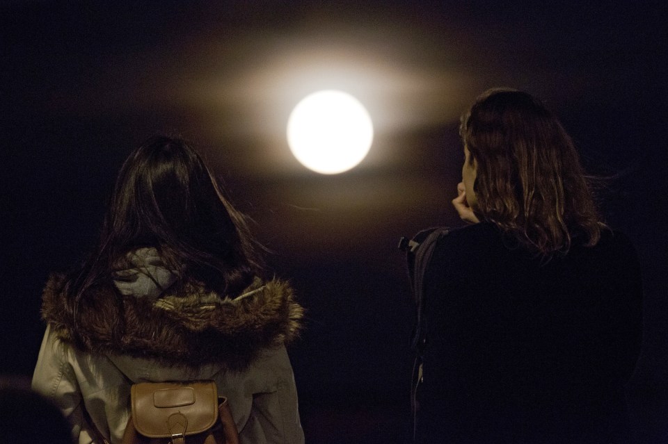  Two women watch the super-bright full moon rise above Lisbon, Portugal