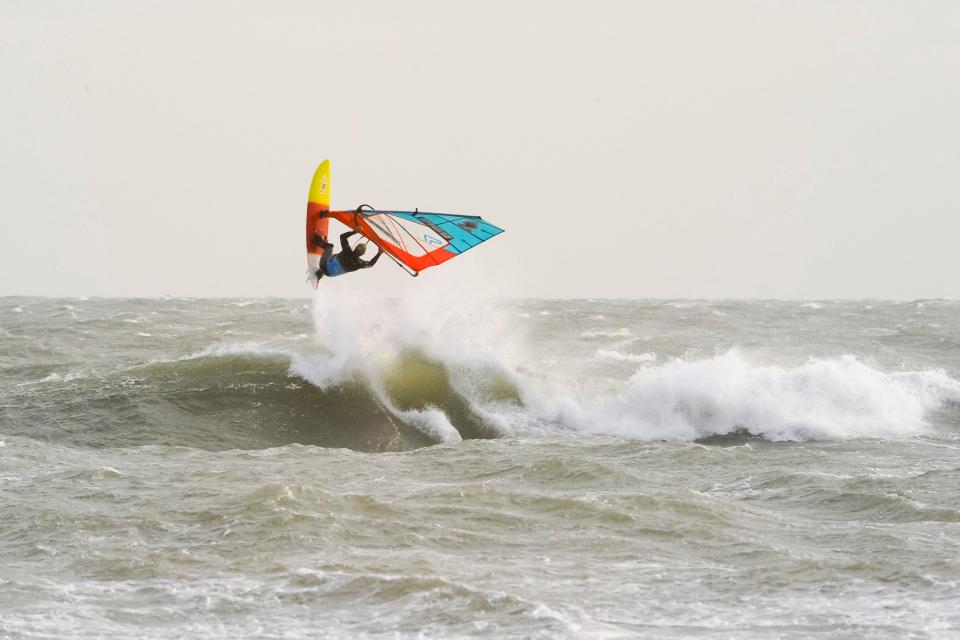  A windsurfer taking advantage of the strong winds and choppy seas off Weymouth Beach in Dorset to do somersaults in the air off the breaking wave