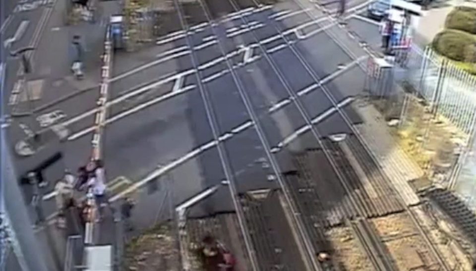  Two women can be seen passing their young children over the barrier of the level crossing