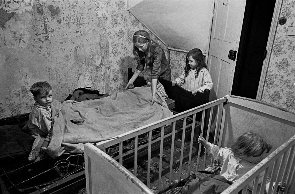  Mrs Milne putting her children to bed, Balsall Heath, 1968: A mother with her three children in a bedroom in disrepair