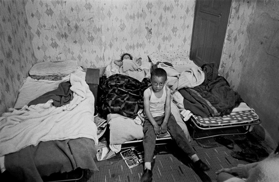  The bedroom of a grossly overcrowded house in Liverpool, 1971. Two children sit in a dirty, cramped bedroom.