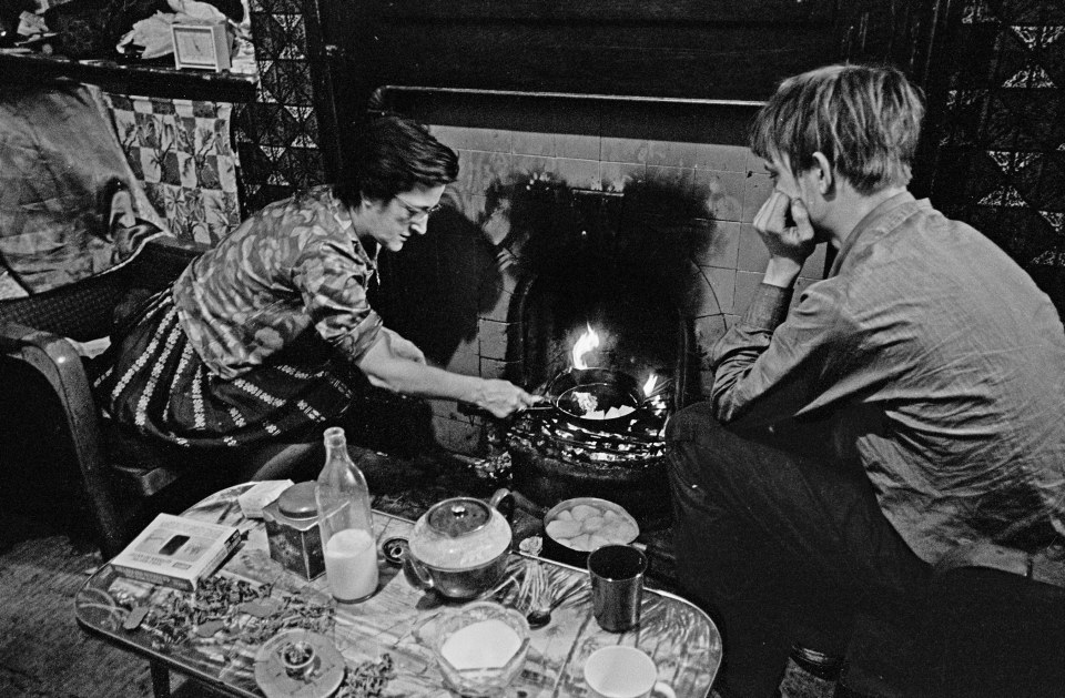  Family living with gas cut off Liverpool, 1970:  A mother cooks on the fireplace as her teenage son watches on