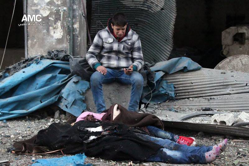  A Syrian boy sitting next to butchered bodies of a young person and child after artillery fire struck his neighbourhood this morning