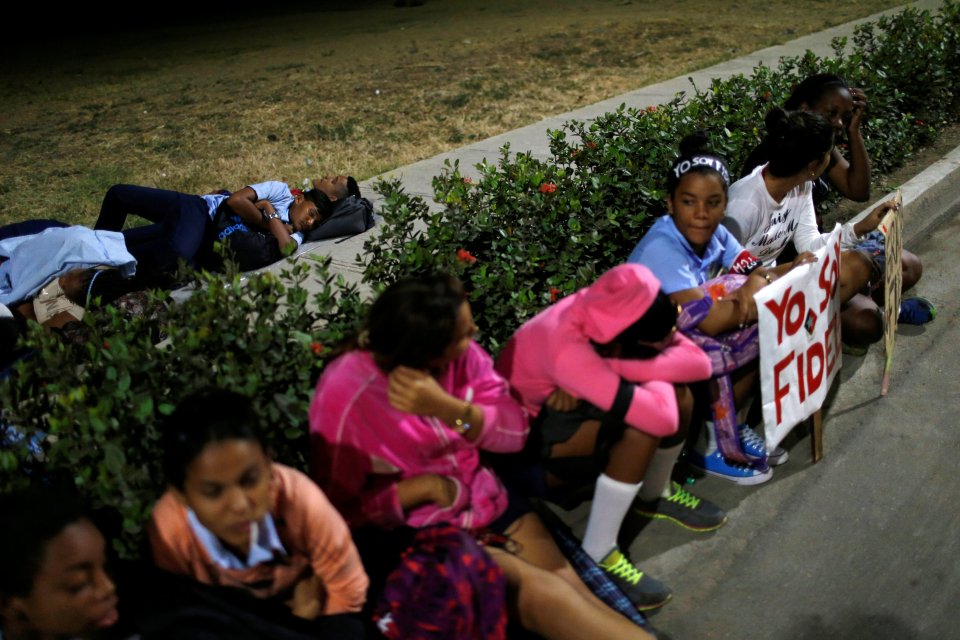  People rest on a sidewalk while waiting for the cortege carrying the ashes to pass