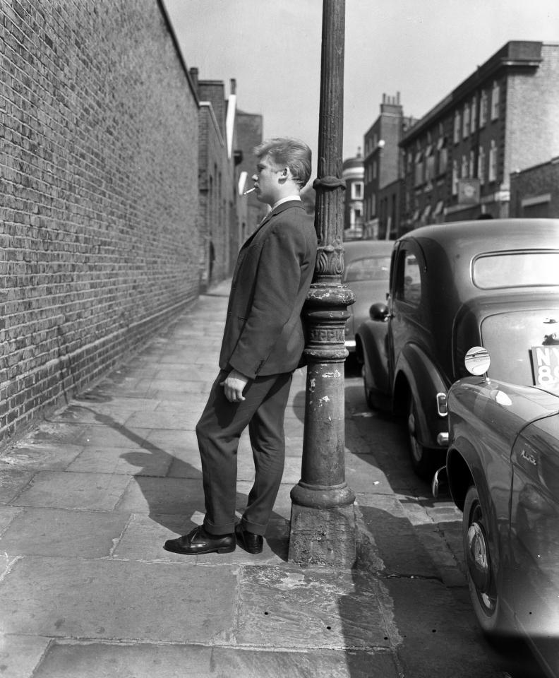  A teenage boy is captured lost in thought while leaning on a lamppost on Gough Street in London