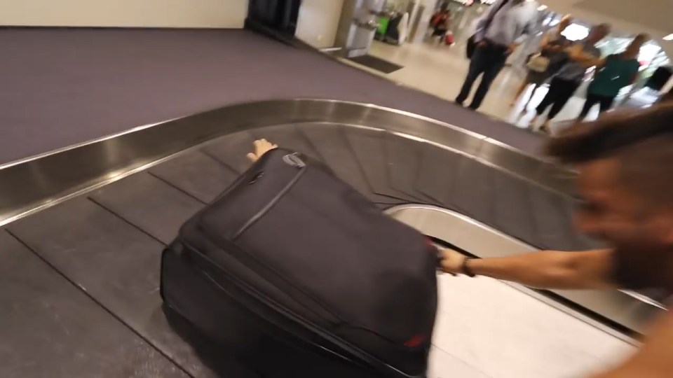 A hand is seen waving from a suitcase on the luggage carousel