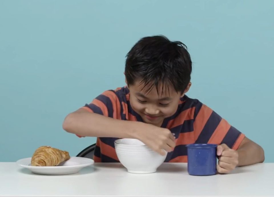 An American boy tucks into a French breakfast of croissant, cereal and hot chocolate 