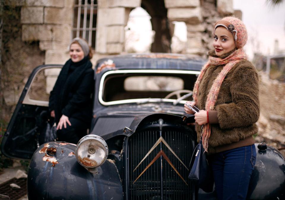  Women pose for a picture with a damaged care at the entrance of the Carlton Hotel