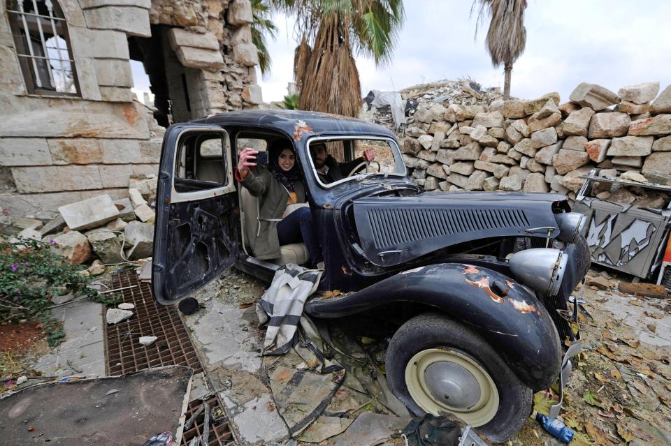  A couple sit inside a damaged vehicle as they take a selfie at the entrance of the Carlton Hotel in Aleppo