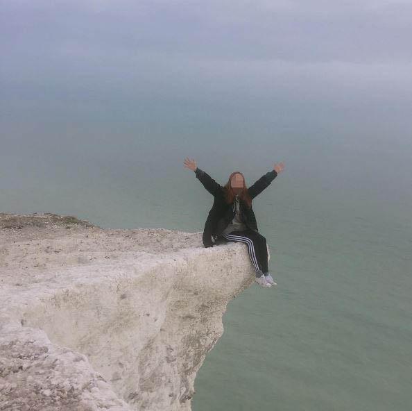  Another woman, wearing black tracksuit bottoms, sits on the edge of the cliff at Seven Sisters with her legs dangling over