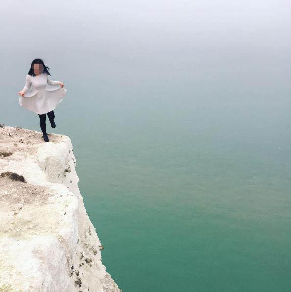  A tourist can be seen in a cream coat as she stand precariously on one leg posing for a picture