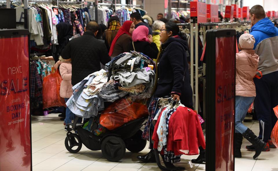  A woman piles dozens of pieces of clothing on a pushchair as she wanders through a NEXT store in Leicester