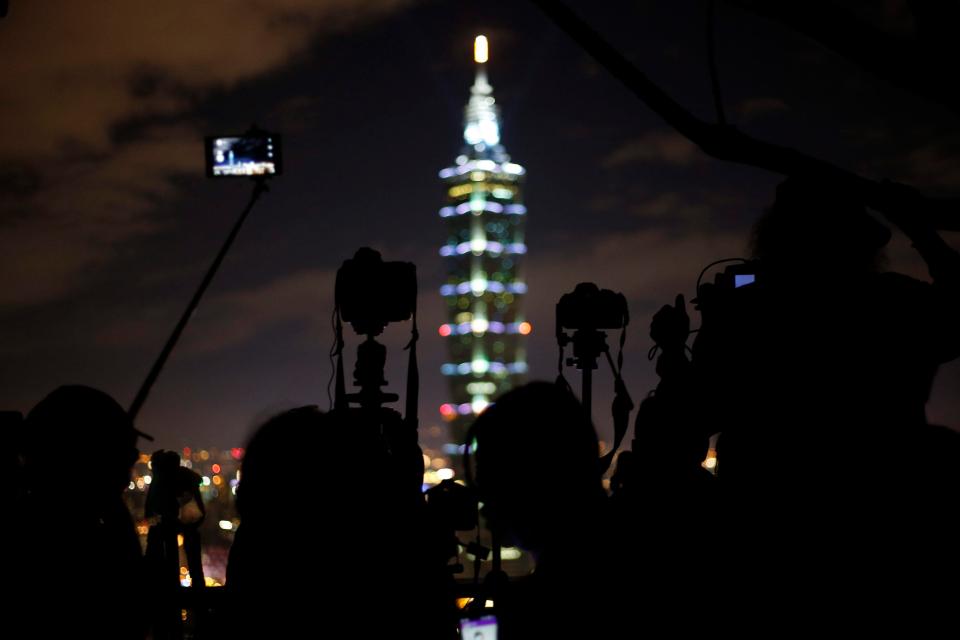  People take photos as they prepare for the fireworks and light effects to illuminate the night sky from the Taipei 101 skyscraper, Taiwan