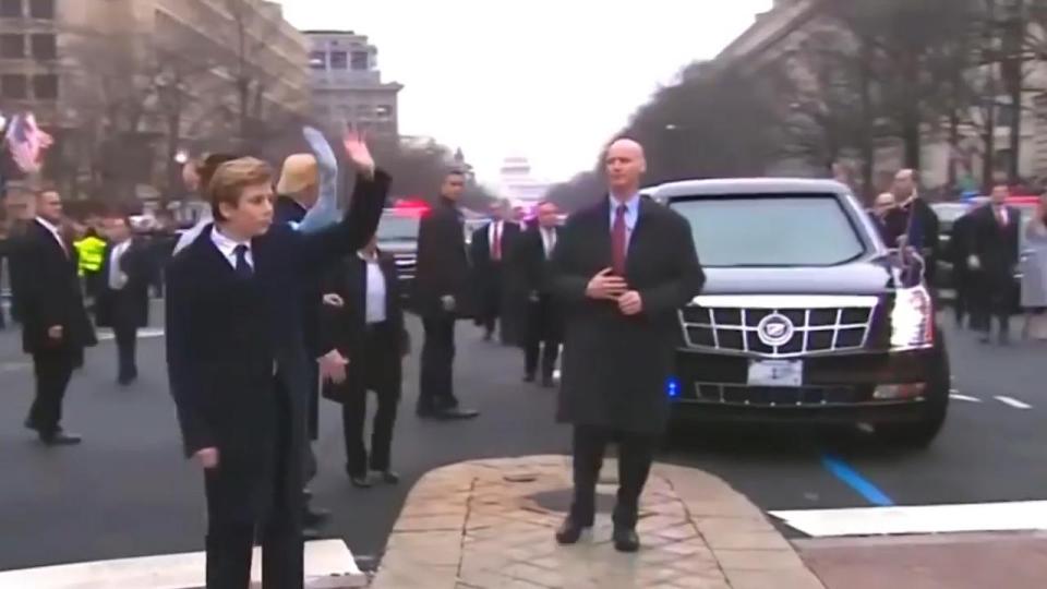  The stern-looking security officer watches on as Barron Trump waves to the cheering crowd