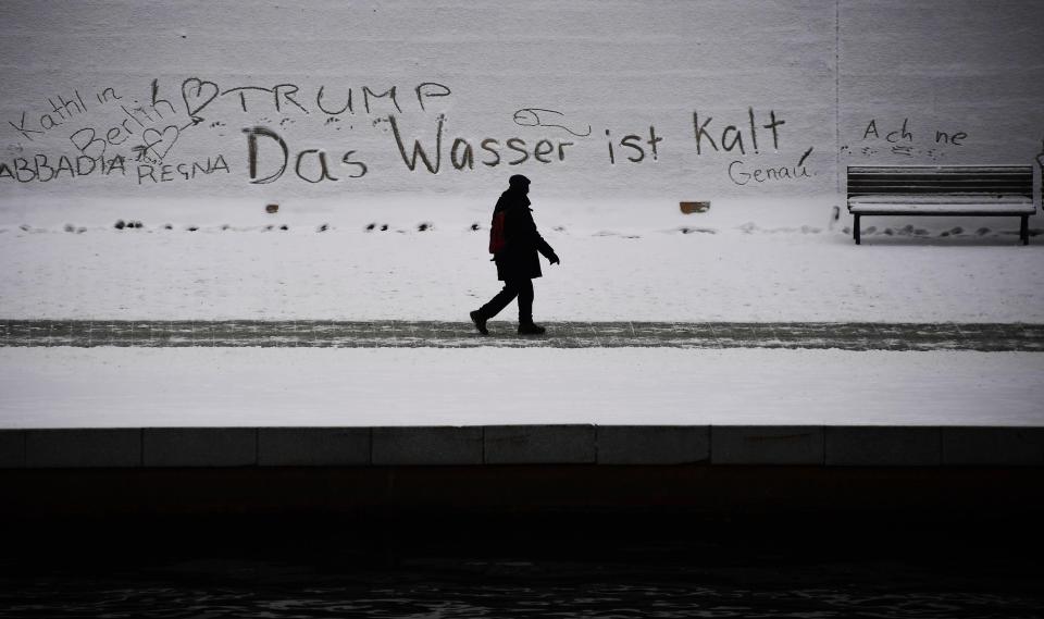  A pedestrian braves the weather as he walks past graffiti, including the line 'the water is cold', in Berlin