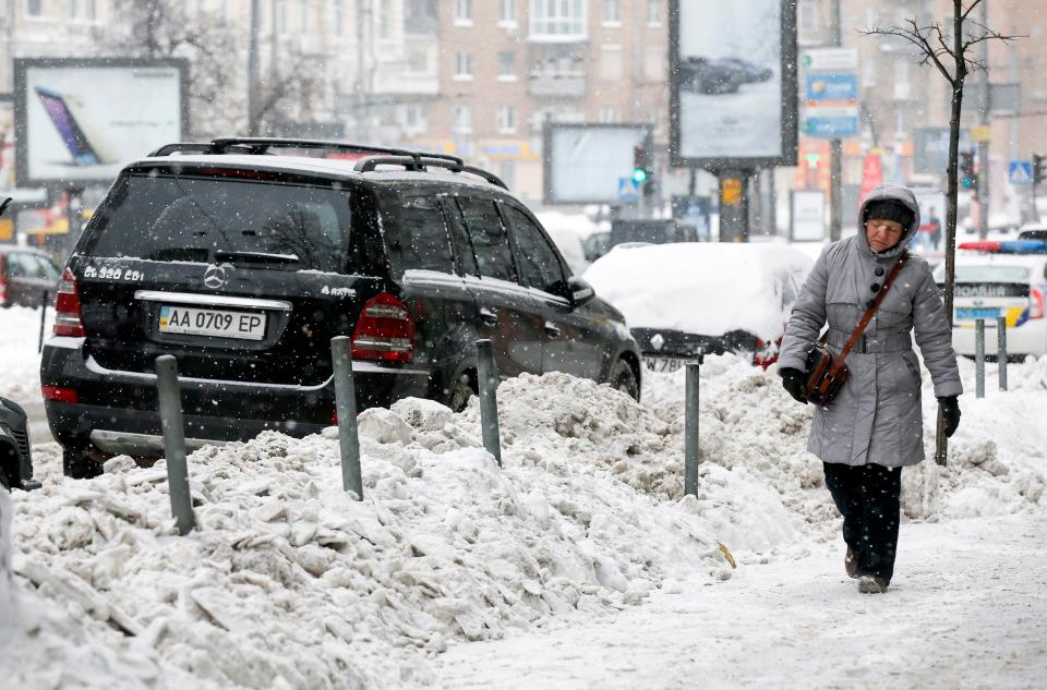  A woman walks past a waist-high snow dump at the side of a road in Kiev, Ukraine