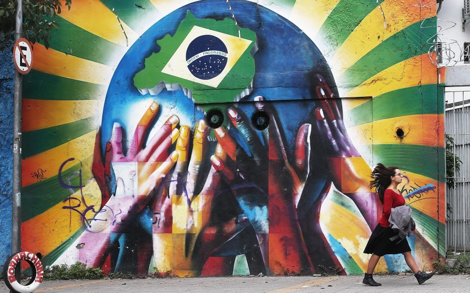  A woman passes graffiti of multi-coloured hands supporting the planet marked with a Brazilian flag in Sao Paulo, Brazil