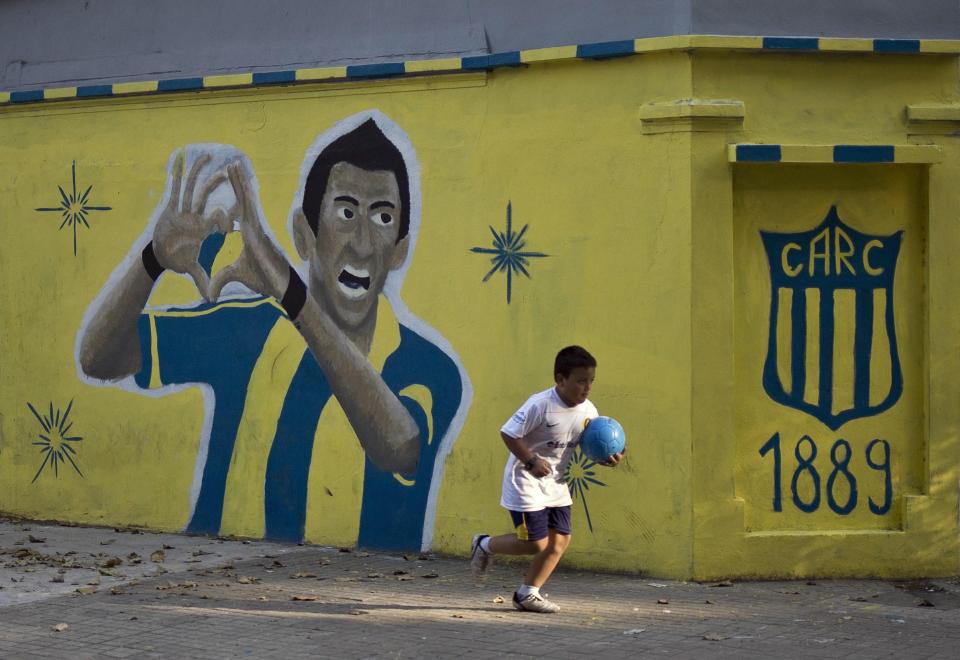  A kid holding a ball runs past a mural depicting Argentine footballer Angel Di Maria painted in a corner near the Gigante de Arroyito stadium of Rosario Central football club in Rosario, Santa Fe province