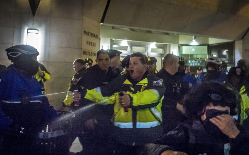  A man unleashes two jets of pepper spay over the crowd as protesters shield their eyes