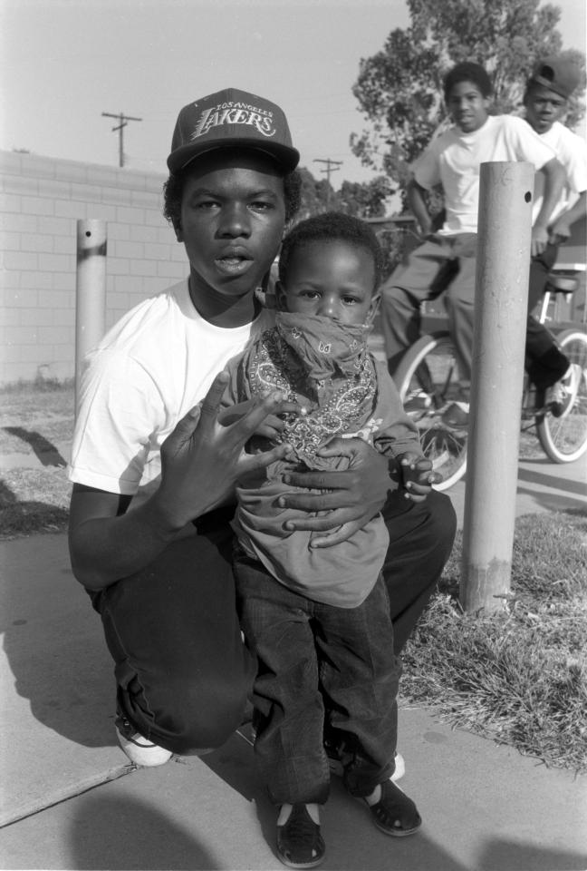  A teenage member of the Crips poses with his little brother draped in the gang's colours