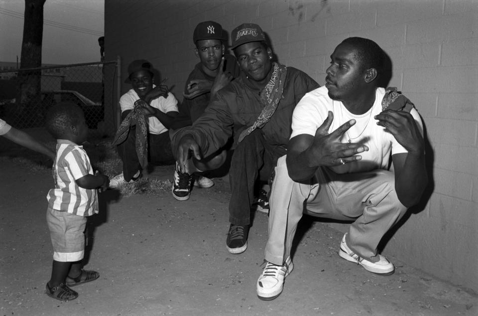  A toddler walks up to a group of gang members posing for the camera