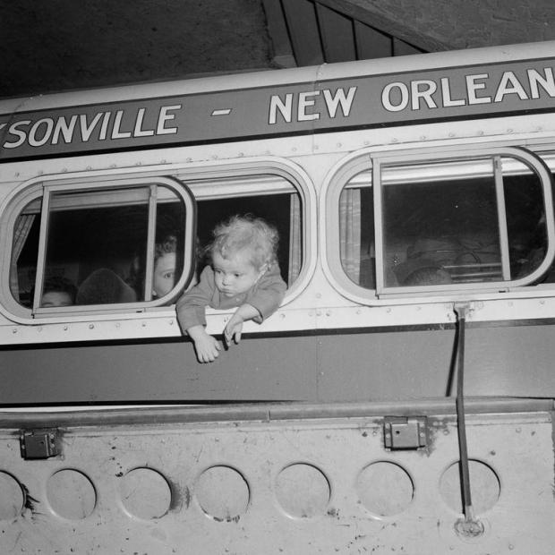 A baby hangs out of the bus window as the bus prepares to leave the station