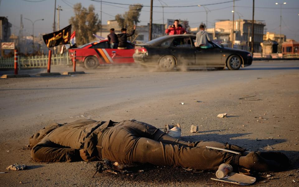  Iraqi youths celebrate a wedding while driving past the body of an ISIS militant