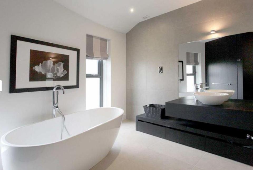  The largest bathroom has a stunning standalone tub inside and a massive mirror behind a modern sink unit