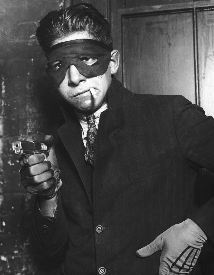  A young gangster with a mask covering his face points his gun at the camera