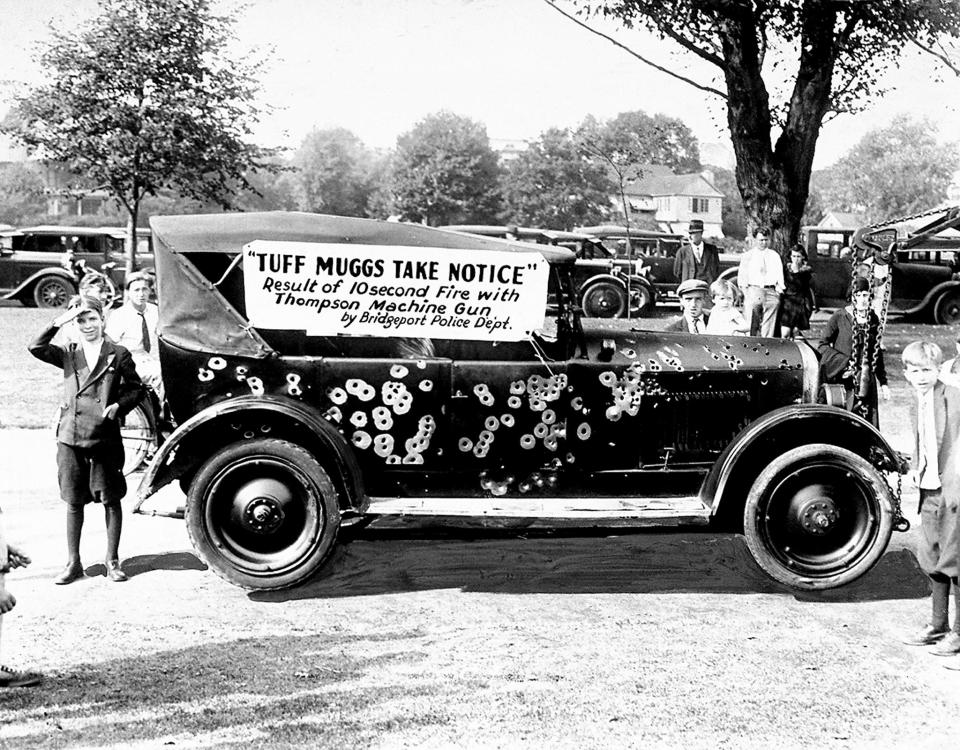  Police and firefighters display a gangster's car riddled by Thompson machine guns