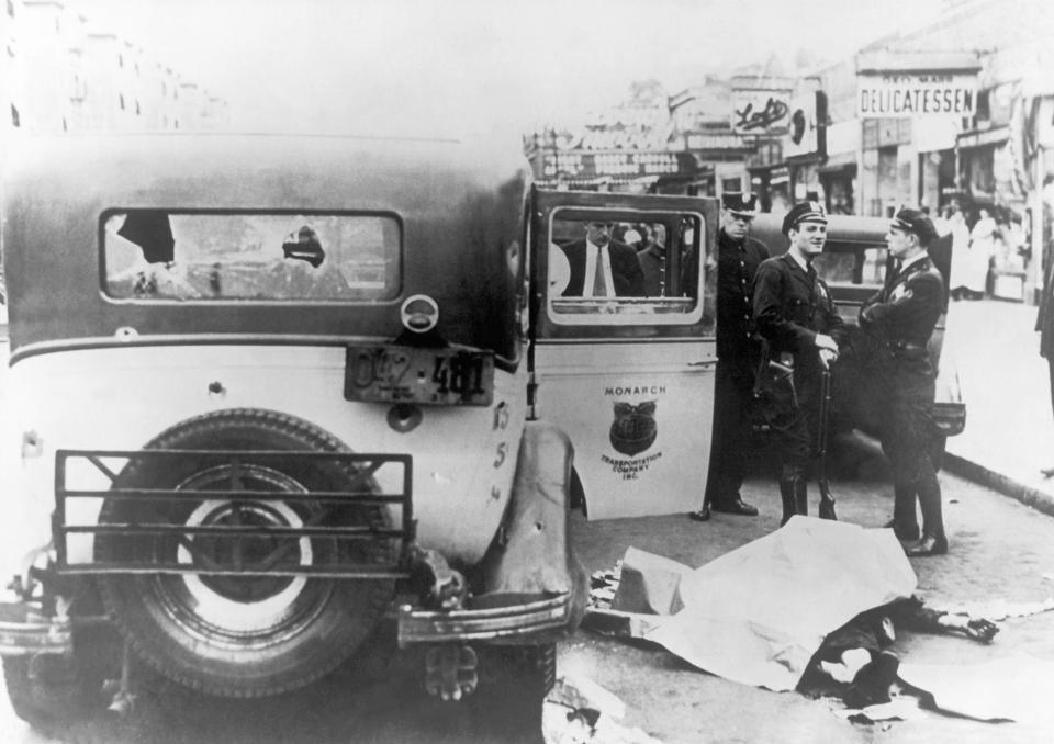  A car riddled with bullet holes is pulled over by police in New York as the corpse of a victim lies in the road