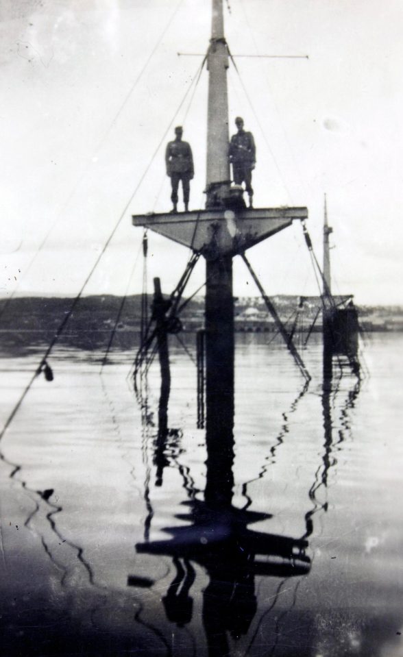  Two crew members perch on the bow of the sunken German destroyer Bernd von Arnim