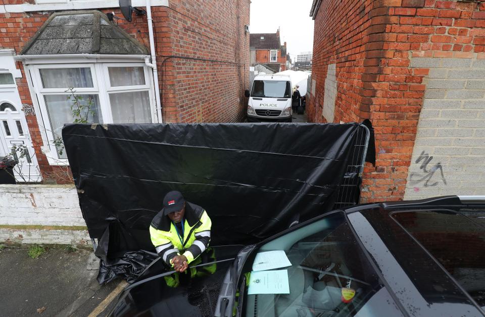  Security guard stands in front of a tarpaulin covering an alleyway by one of the houses