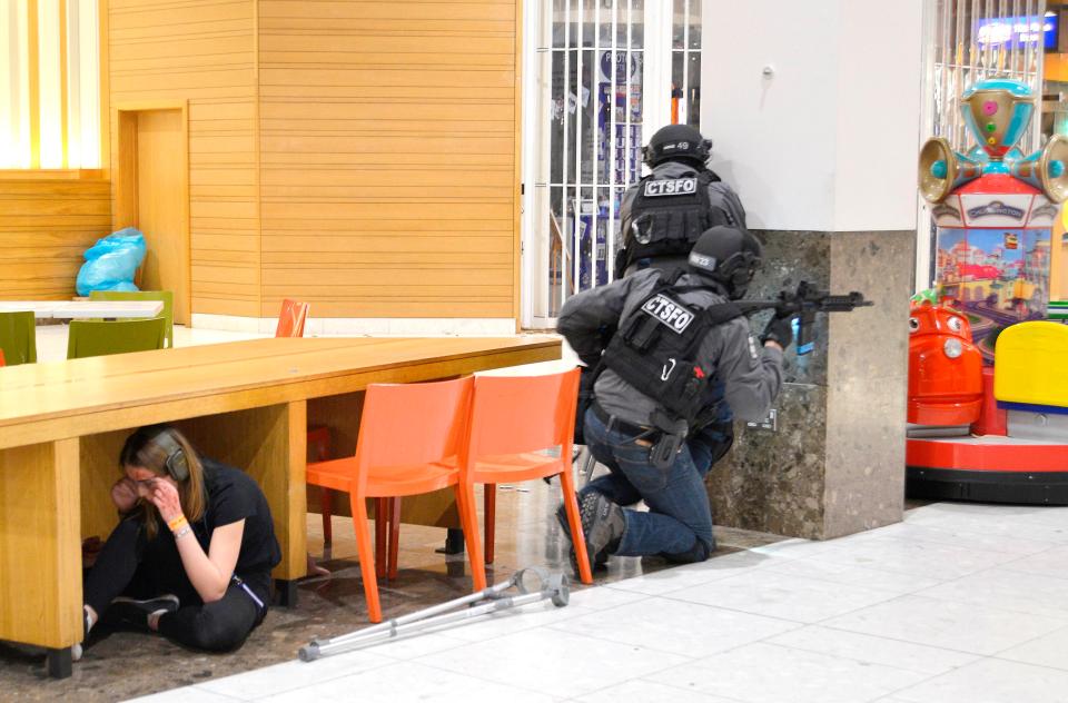  A woman appears to be hiding under a table in the food court as two armed cops stand close by