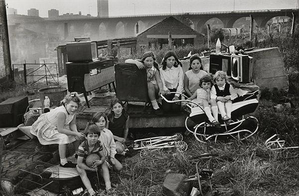  ‘Children with collected junk near Byker Bridge, 1971’. Nine kids are captured in a makeshift playground. One boy hugs a football, while two girls are seated in a pram