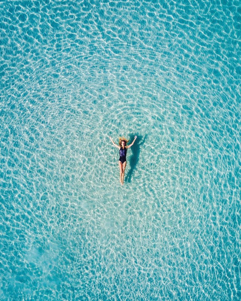 A swimmer appears suspended vertically in the cool blue ocean of Silver Sands, Aldinga Beach, when captured from directly above