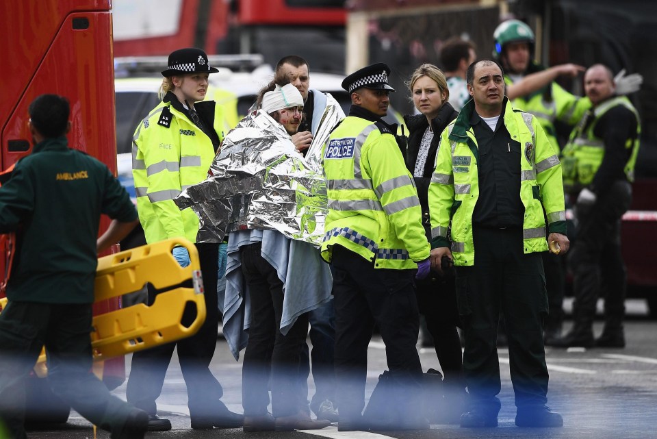 A victim is treated by paramedics and wrapped in a foil blanket as he explains to officers what he saw