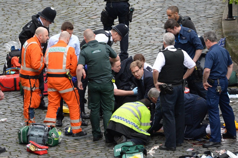 Conservative MP Tobias Ellwood, centre, helps emergency services attend to a police officer outside the Palace of Westminster