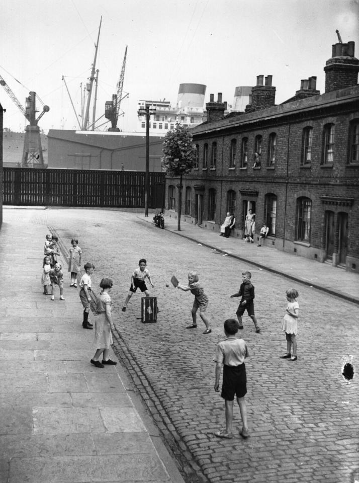  Children playing cricket in a street in Millwall, east London on August 15, 1938, with a large liner in the background