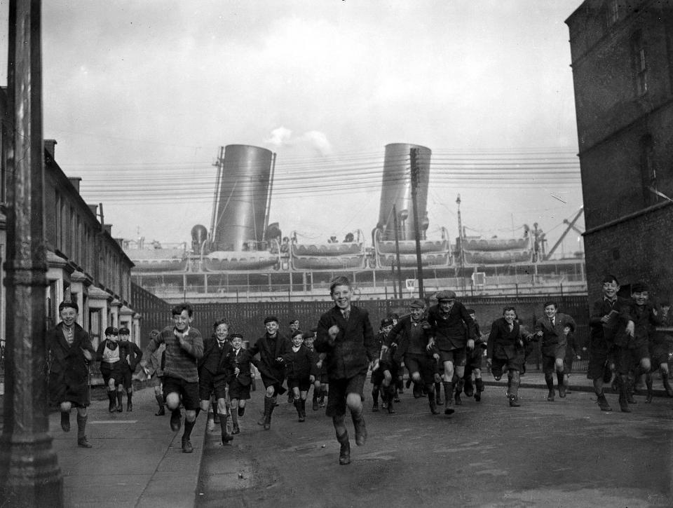  Children pour out of their School in Drew Street, Silvertown, in the east end of London, with the liner ,Rajputana in the background on January 15, 1932