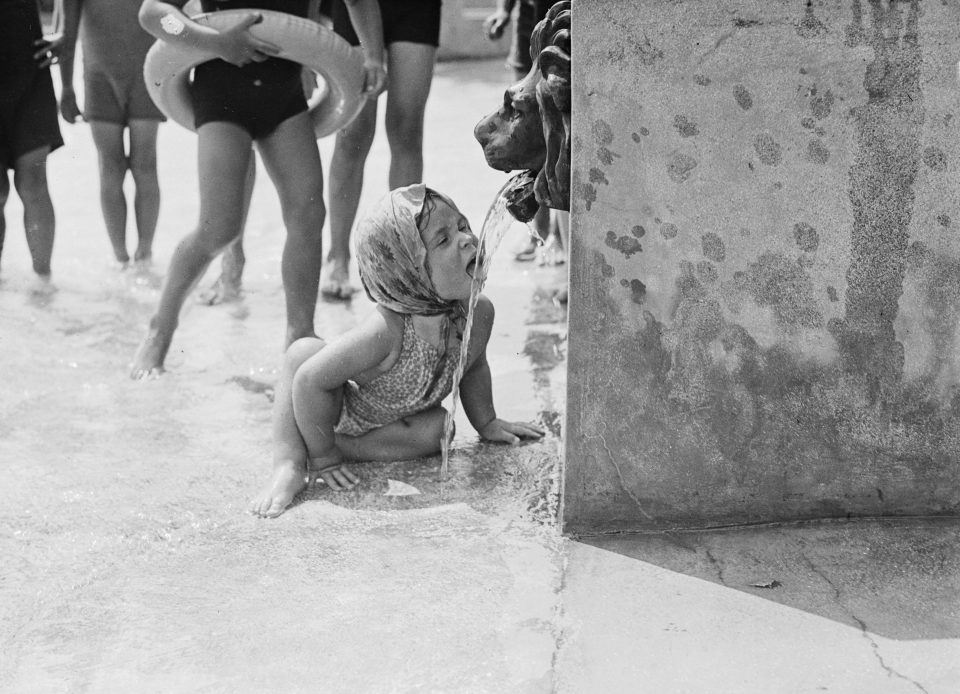  A photograph of a little girl drinking from a fountain with a lion's head at Finchley Swimming Pool, London in 1937