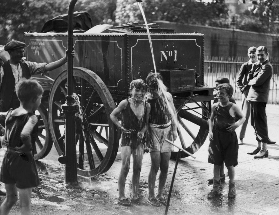  A water cart man turns the water main on a group of boys to help them cool off in a street in Westminster during a heatwave in August 1930