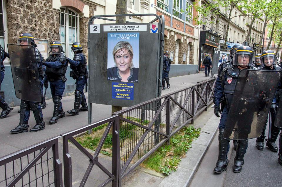  Riot police stand next to another defaced poster as they block the road